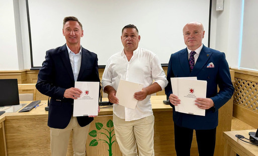 trzech mężczyzn pozuję do wspólnego zdjęcia, w rekach trzymają teczki z podpisanymi umowami